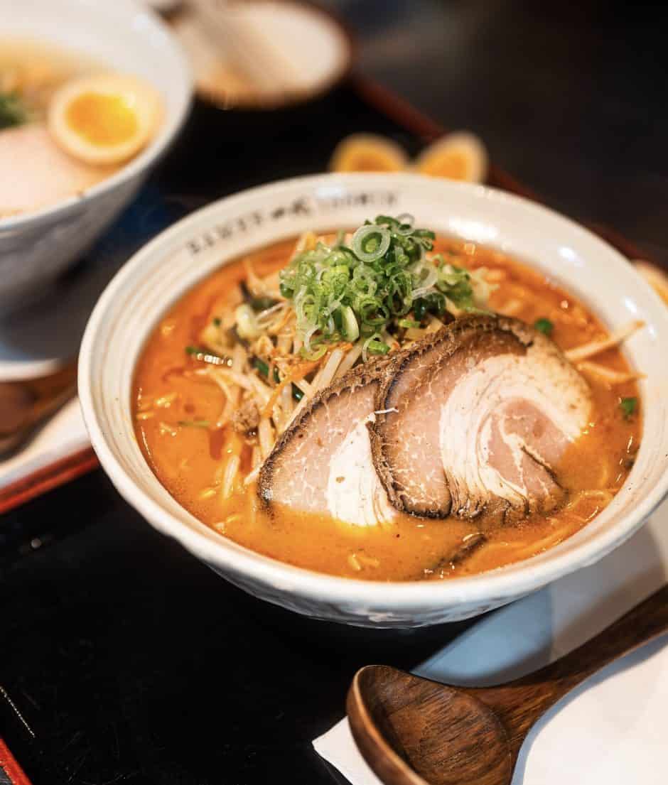Savory bowl of spicy ramen with pork, green onions, and broth, served with boiled eggs in a cozy Asian restaurant.
